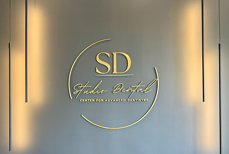 The image shows a sign with gold lettering on a silver background, featuring the logo of SD Studio Dental and the text Center for Advanced Dentistry.
