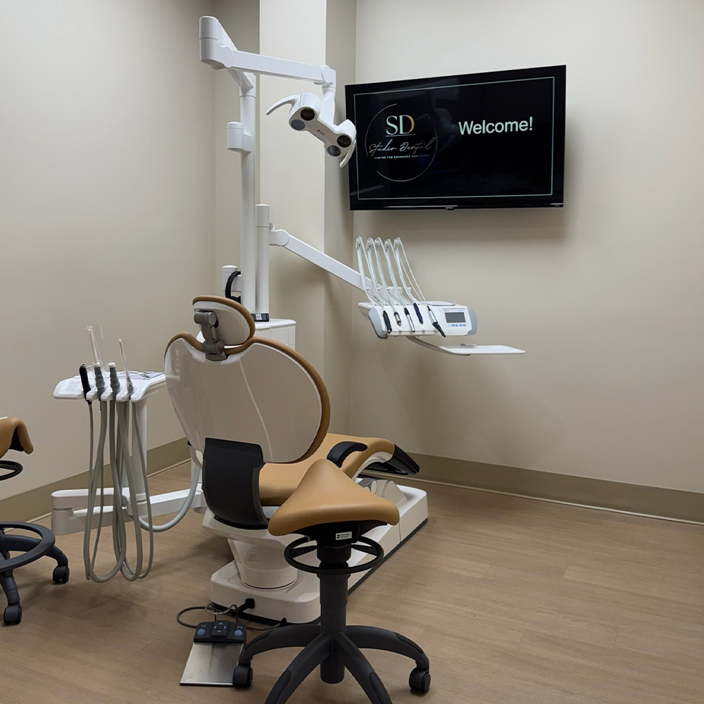 A dental office setting featuring a dental chair with adjustable equipment, a monitor displaying a SD logo, and a welcome sign on the wall.